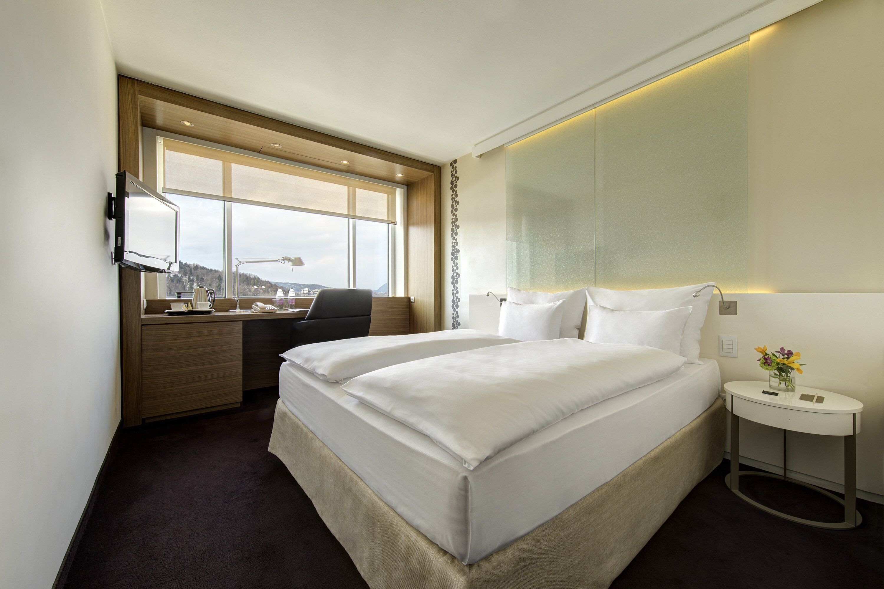Una habitación de hotel con una cama grande, un escritorio, una silla, un televisor y una ventana con vista a la ciudad.