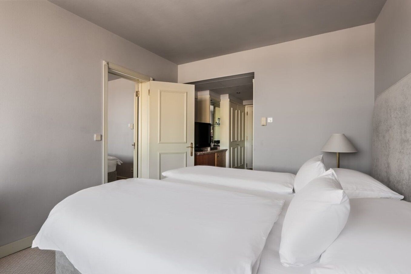 Een hotelkamer met twee eenpersoonsbedden, een nachtkastje, een lamp en een deur naar een badkamer.