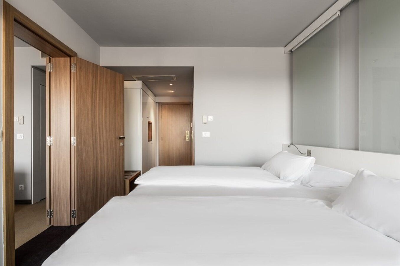 A hotel room with two beds, wooden wardrobe, and a large window.