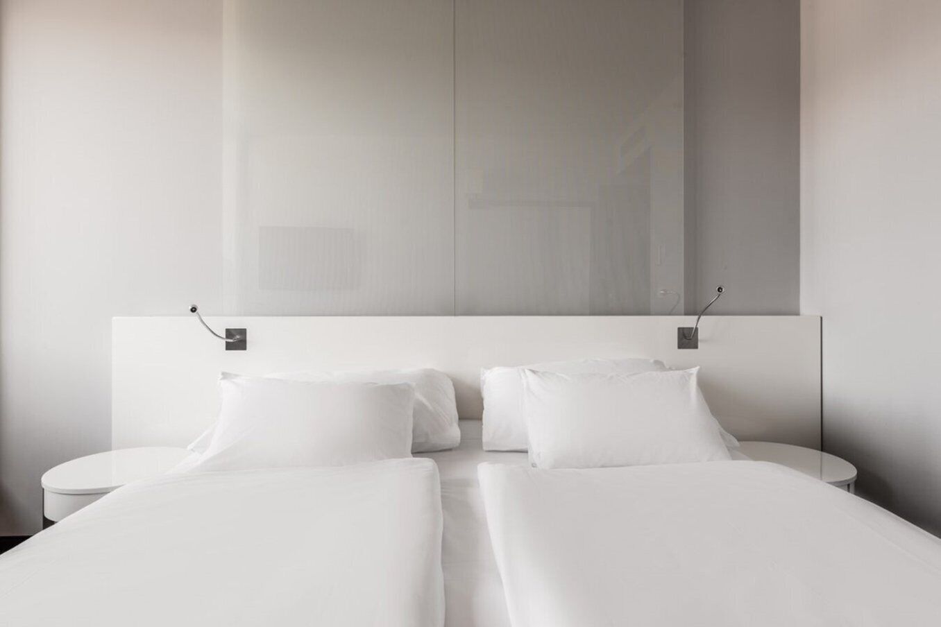 Una habitación de hotel moderna con una cama grande, dos mesitas de noche y un espejo grande sobre la cama.