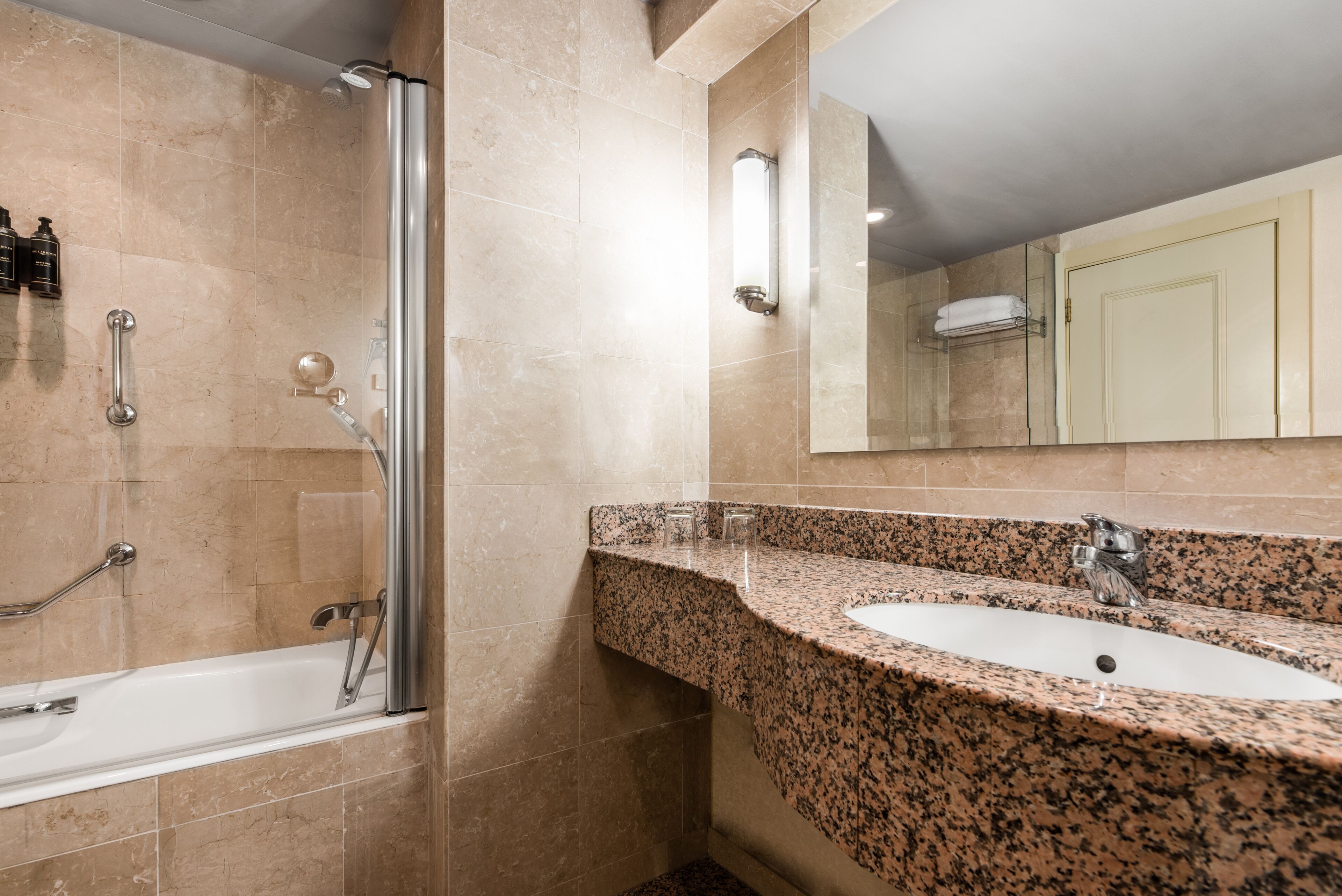 Une salle de bain moderne avec un lavabo sur un plan de travail en granit, une douche en verre et une barre d’appui.