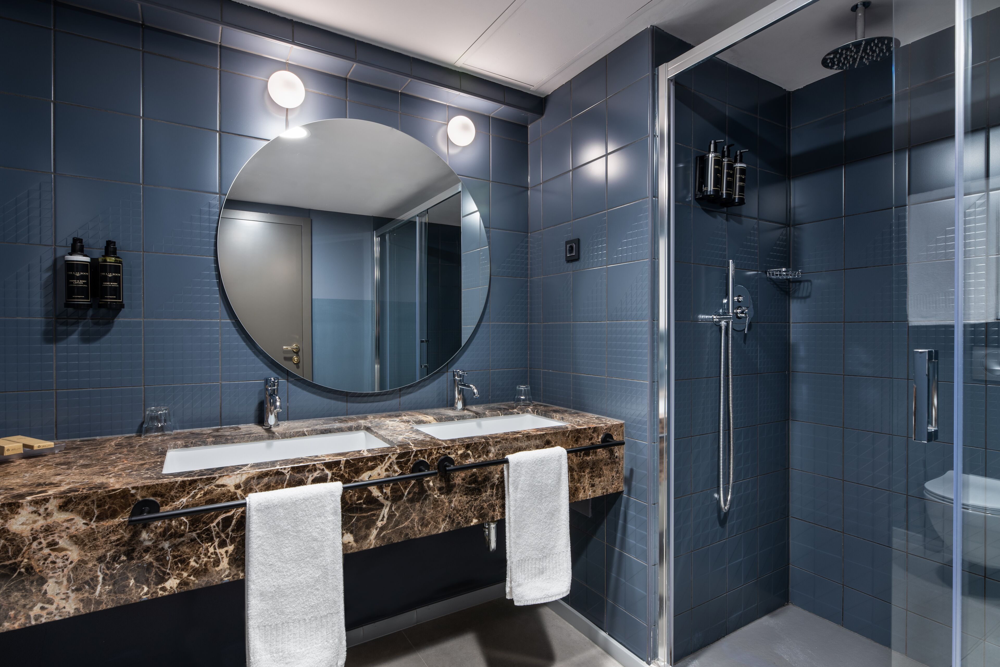 Une salle de bain moderne avec un lavabo en marbre, un grand miroir et une douche à parois de verre.