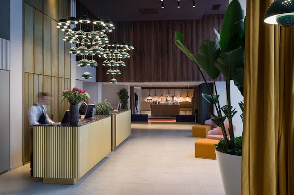A modern reception area with a wooden reception desk, multiple hanging pendant lights, and a seating area with yellow cushions.