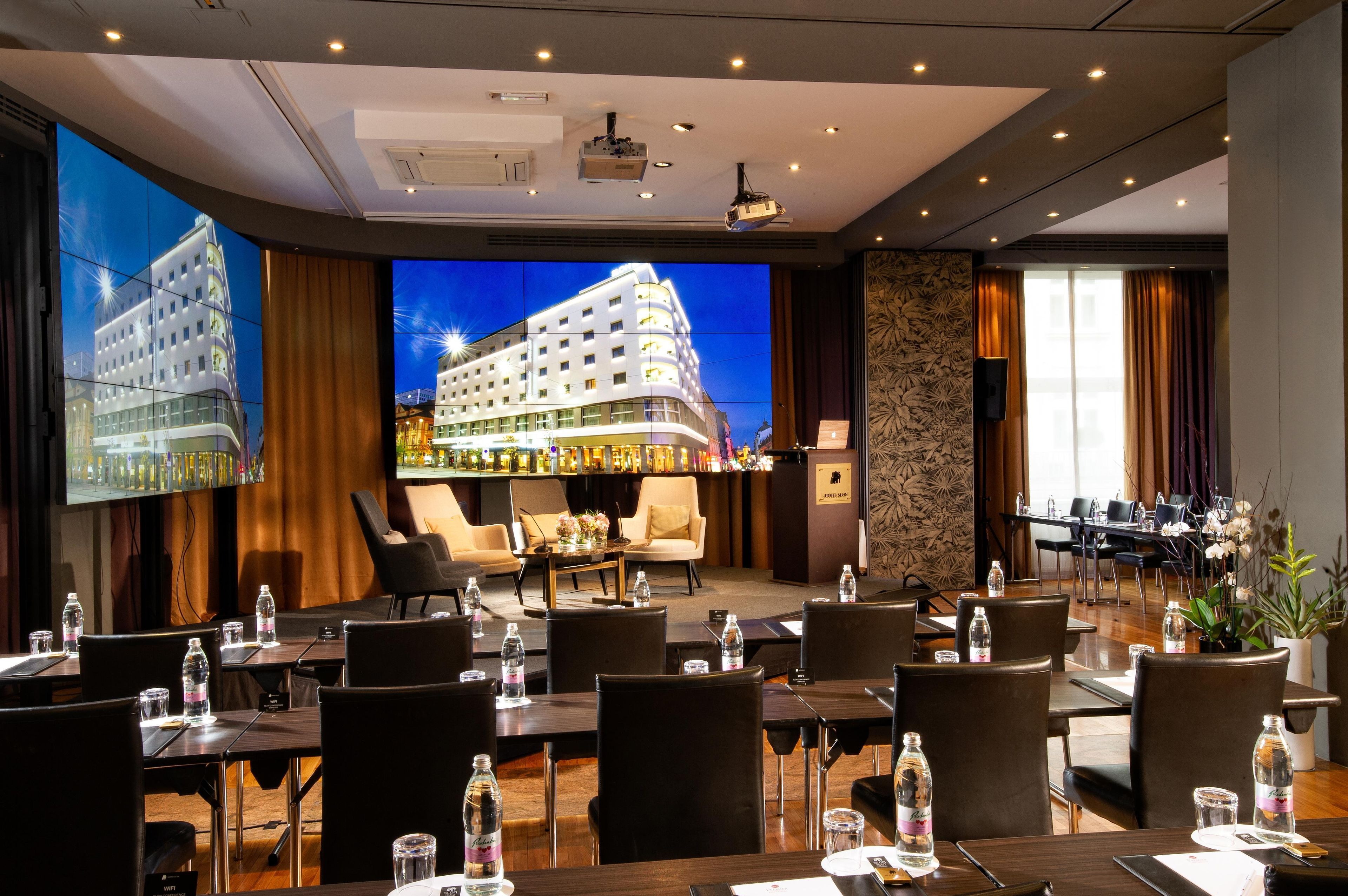 A hotel conference room with multiple tables, chairs, and a large screen displaying a building.