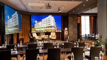 A hotel conference room with multiple tables, chairs, and a large screen displaying a building.