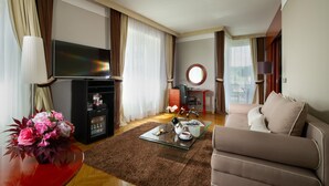 Une chambre d’hôtel avec un canapé, une télévision, une petite table ornée d’un vase de fleurs, un réfrigérateur et un bureau avec une chaise.