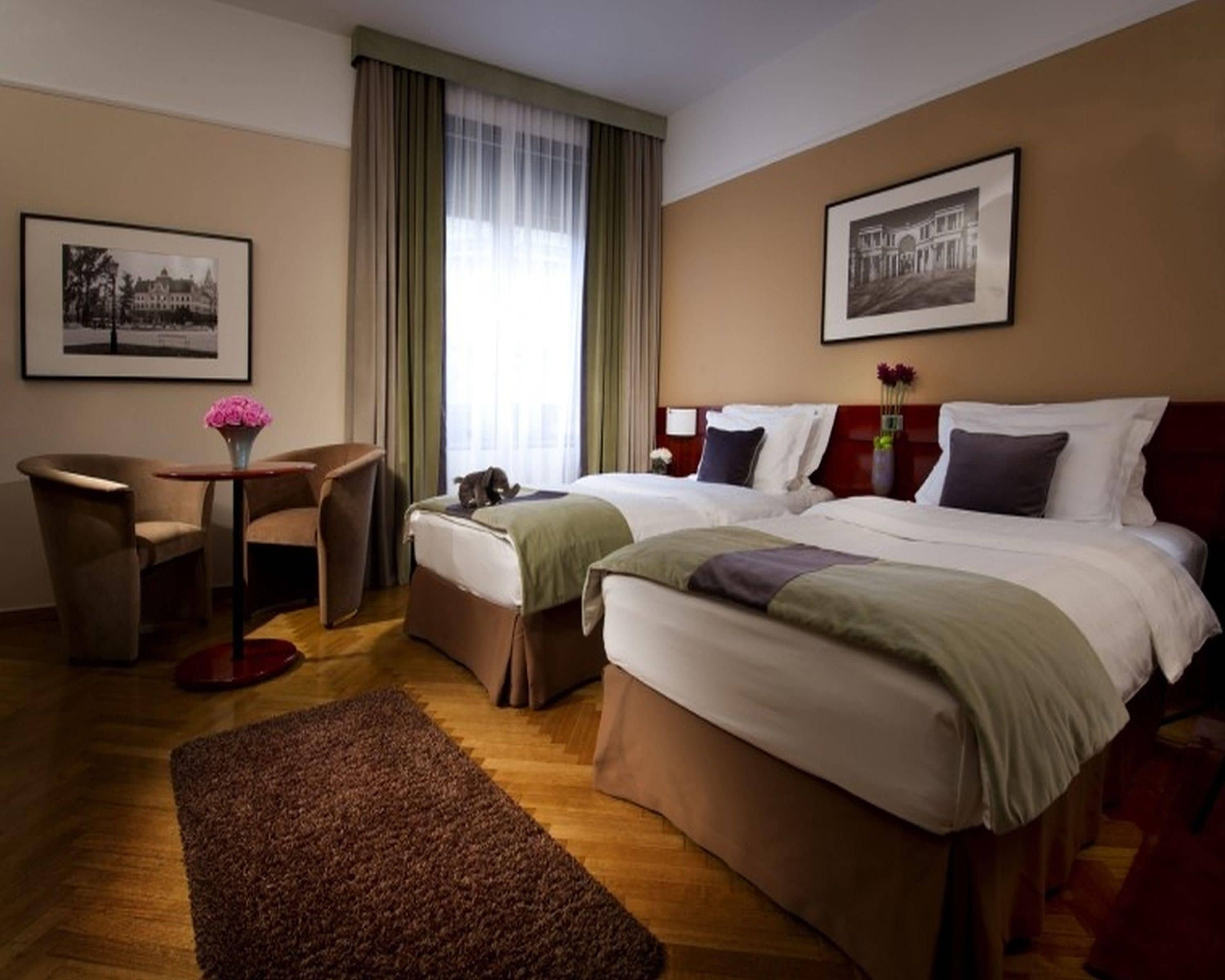 Ein Hotelzimmer mit zwei Betten, einem Schreibtisch, einem Sessel, einem Teppich und zwei gerahmten Bildern an den Wänden.