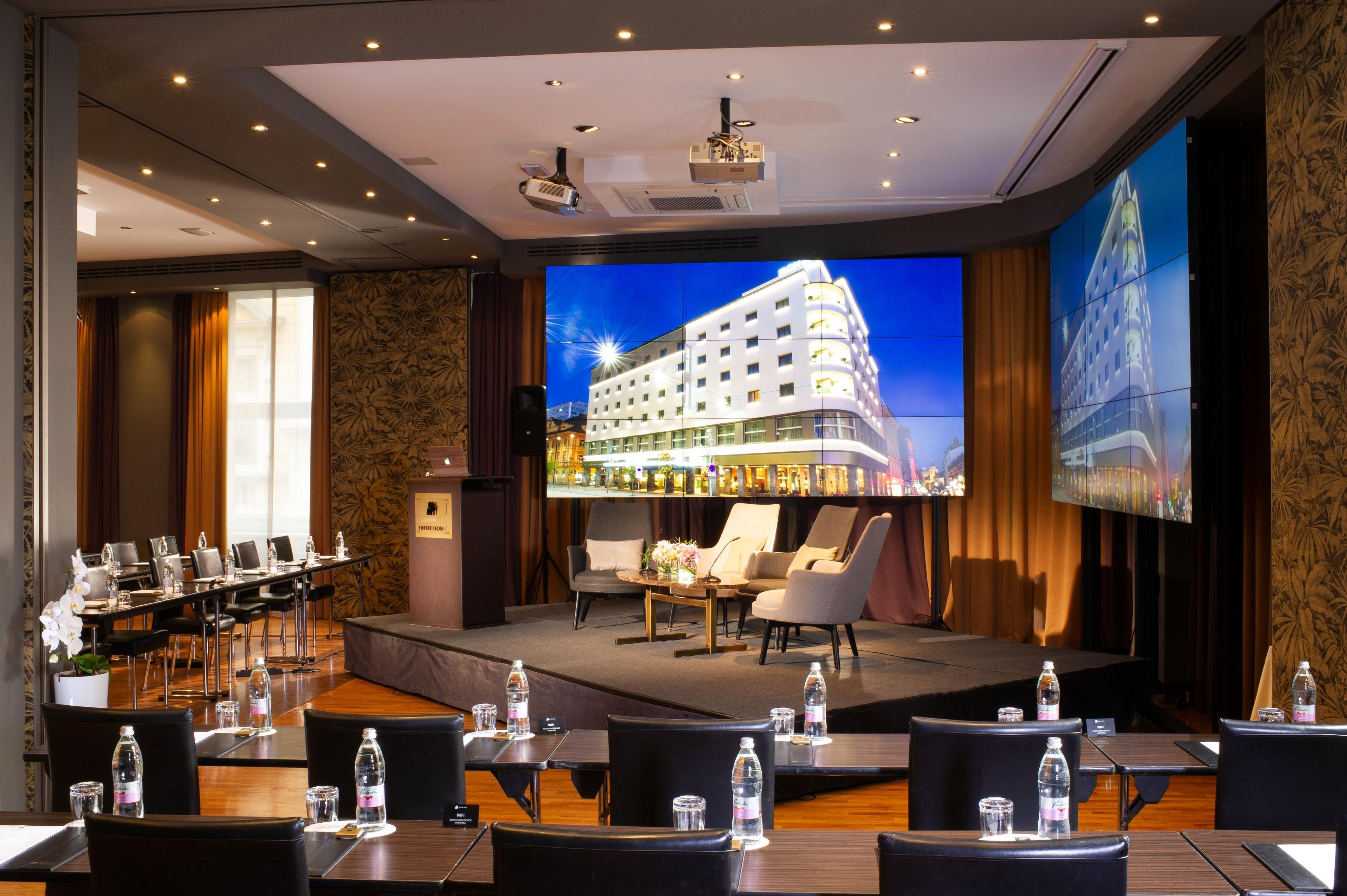A hotel conference room with a stage, projection screen, and seating for presentations.