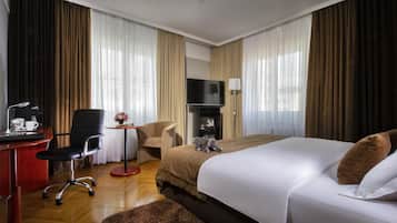 A hotel room with a bed, a desk with a chair, a television, and a small table with a lamp.