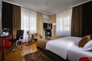 Een hotelkamer met een bed, een bureau met stoel, een televisie en een tafeltje met een lamp.