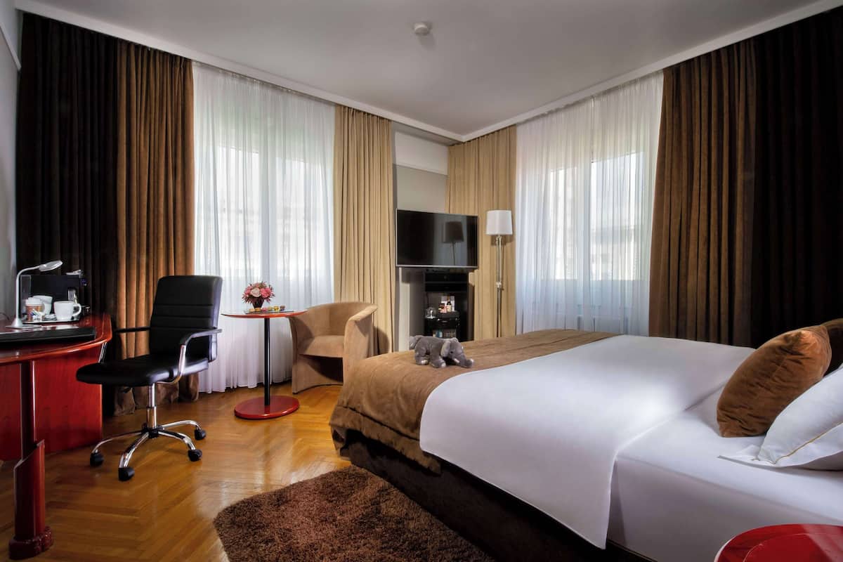Une chambre d’hôtel avec un grand lit, un bureau avec une chaise, une télévision et une petite table avec une lampe.