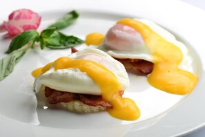 Une assiette blanche contenant deux œufs pochés, de la sauce hollandaise et des lardons.