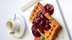 Een wafel met bessencompote en een kop koffie op een wit bord.