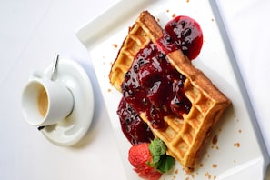 Un gaufre garnie de compote de fruits des bois et une tasse de café, le tout présenté sur une assiette blanche.