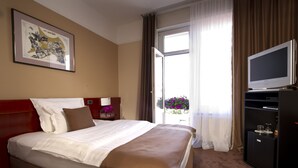 Une chambre d’hôtel avec un grand lit, une télévision, une petite armoire et une fenêtre avec des rideaux.