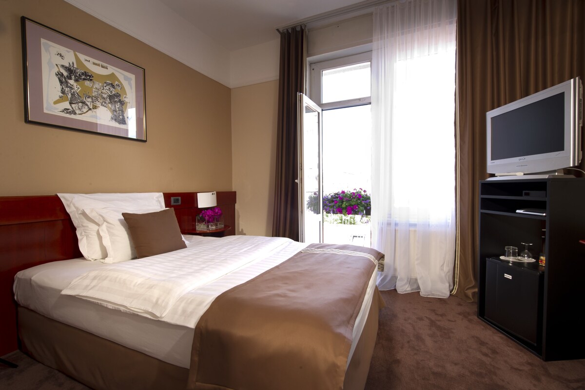 Une chambre d’hôtel avec un grand lit, une télévision, une petite armoire et une fenêtre avec des rideaux.