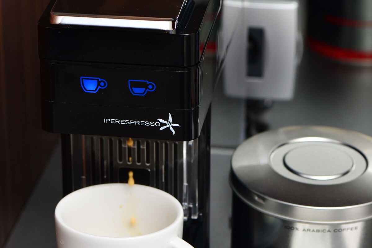 Une machine à café verse du café dans une tasse, avec une dosette de café et un récipient portant l'inscription « illy » à proximité.