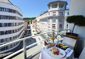 A balcony with a table set for breakfast, overlooking a city street with buildings and a clear sky.