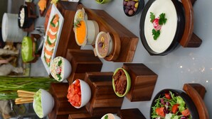 Diverse gerechten, zoals sushi, salades en andere hapjes, gepresenteerd op houten plankjes en in schalen.
