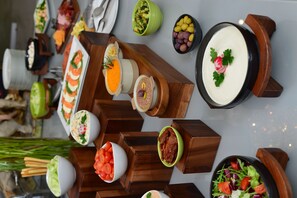 Une variété de plats présentés sur des présentoirs en bois et dans des bols, notamment des sushis, des salades et d’autres amuse-gueules.