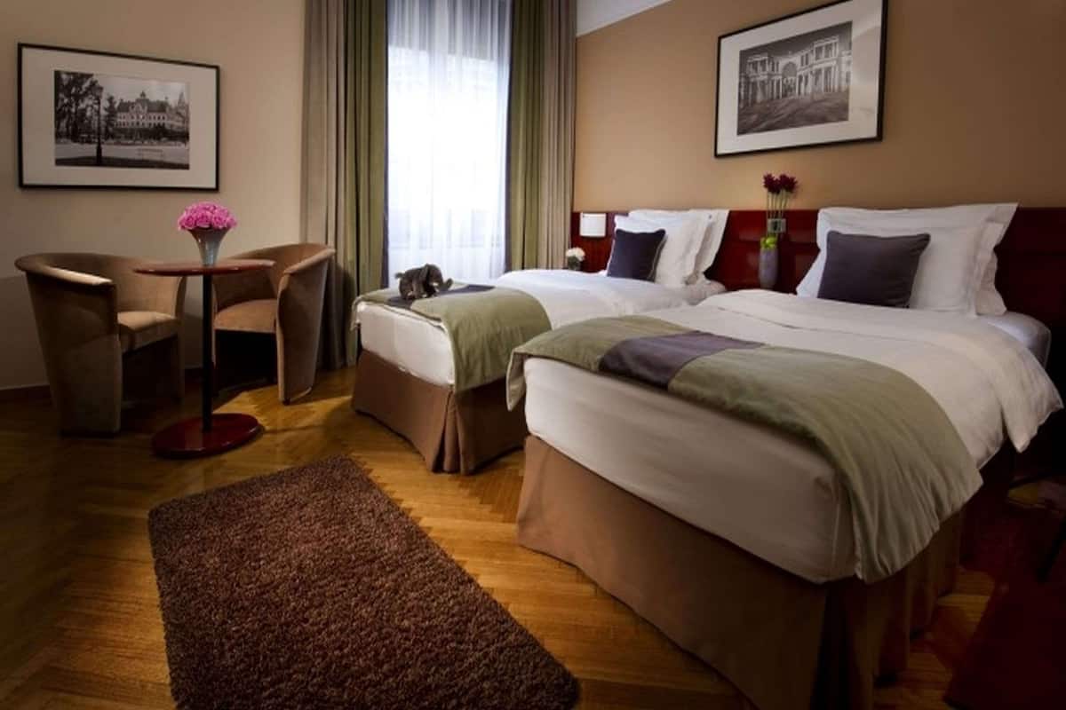 Une chambre d’hôtel avec deux lits, un bureau, une chaise et une grande fenêtre avec des rideaux.