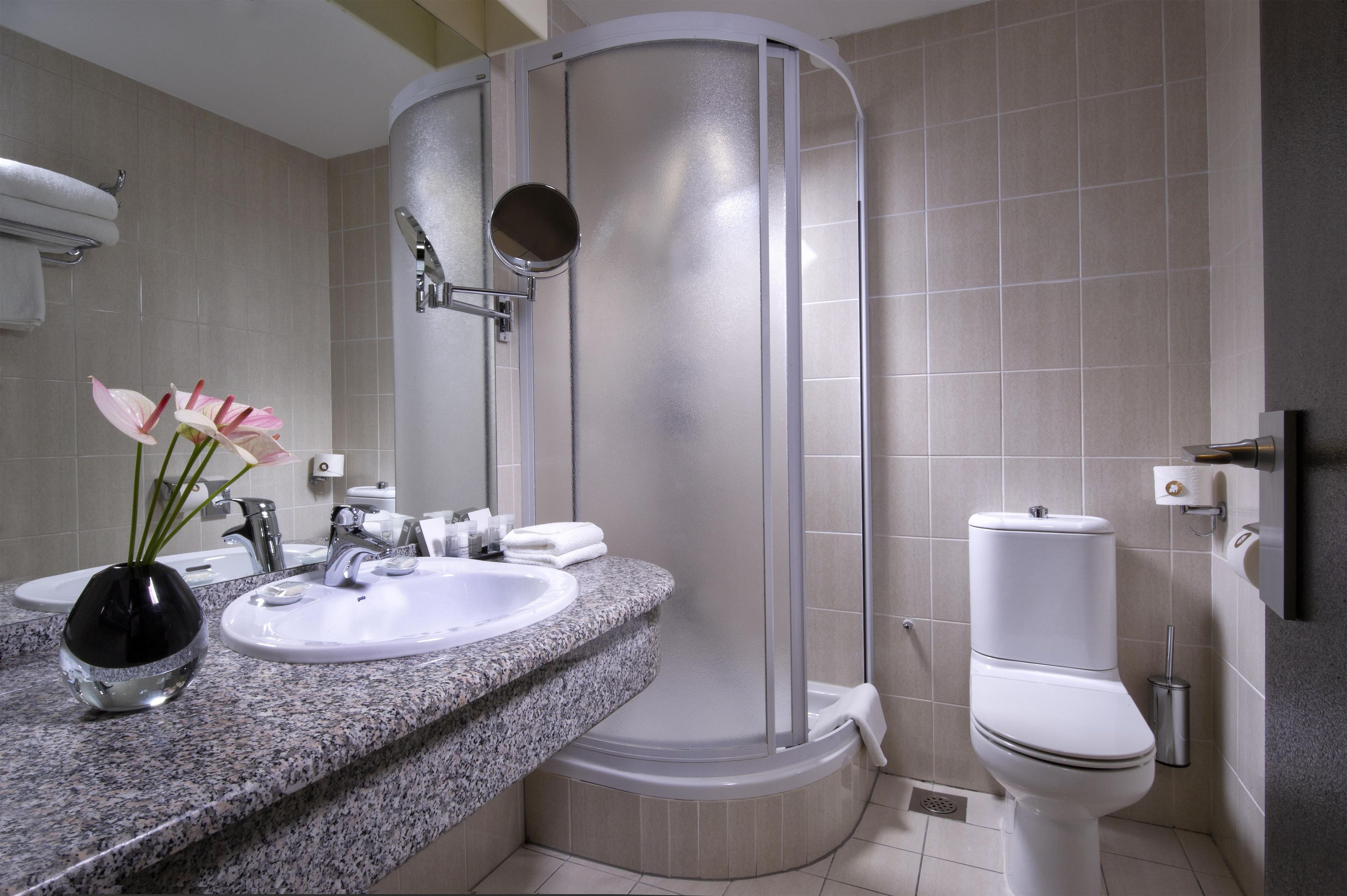 A modern bathroom with a granite countertop, a white sink, a toilet, and a glass-enclosed shower.