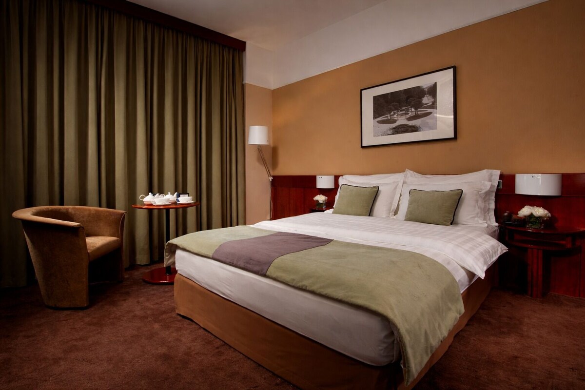 Une chambre d’hôtel avec un grand lit, une chaise, une table avec un service à thé et un tableau encadré au mur.
