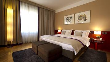 Habitación de hotel con una cama grande, un escritorio, una silla, una mesita con un florero y dos lámparas de pared.