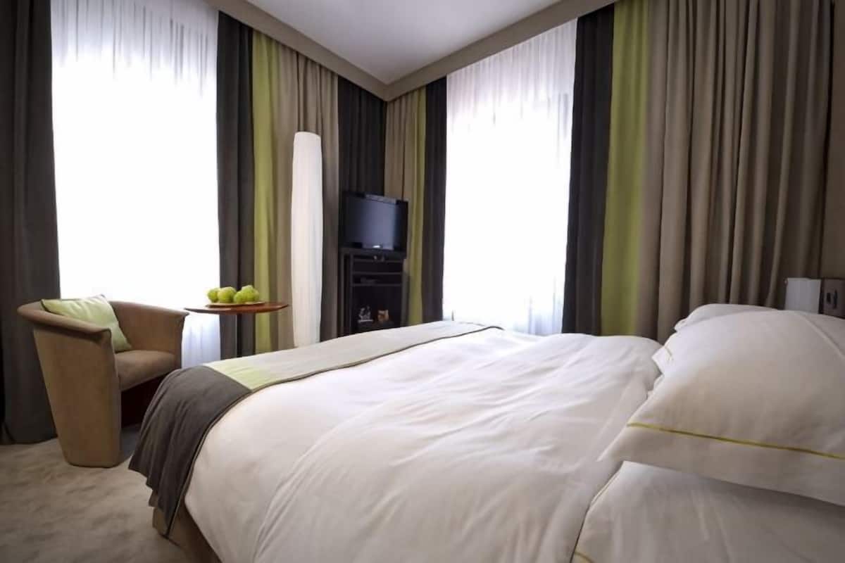Une chambre d’hôtel avec un grand lit, une chaise, une petite table avec des fruits et un téléviseur.