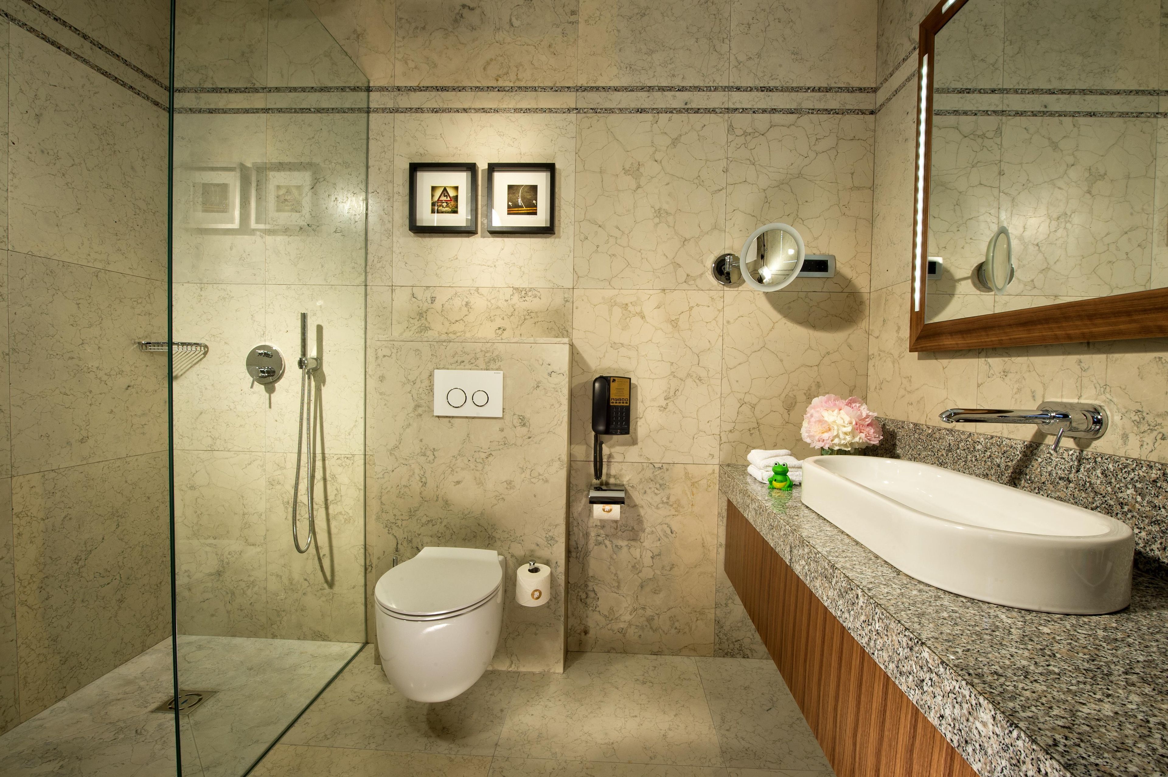 A modern bathroom with a glass-enclosed shower, a toilet, a sink with a granite countertop, and a mirror.