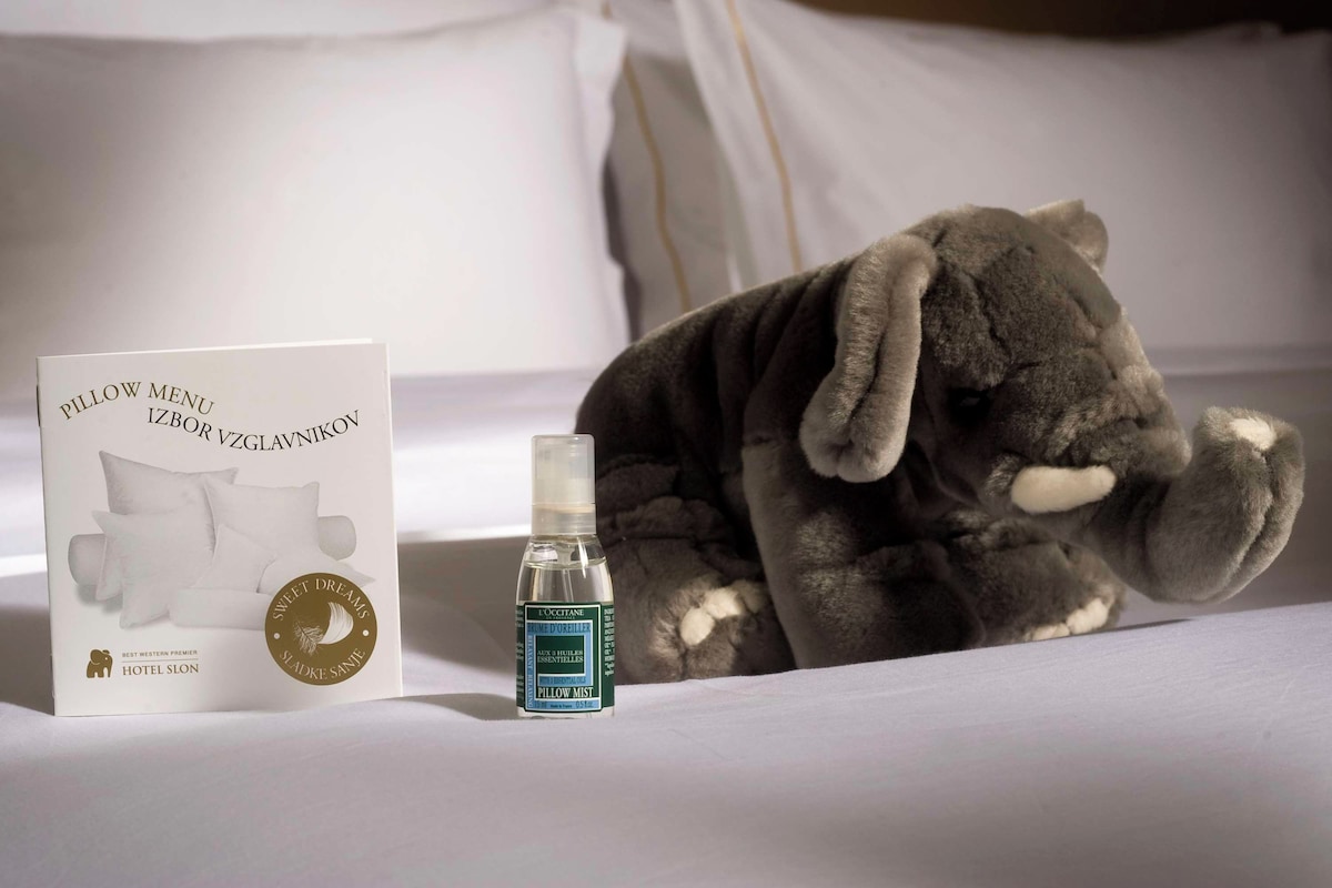 A pillow menu, a bottle of pillow mist, and a plush elephant toy on a bed.
