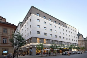 Un hotel de varios pisos con fachada moderna, zona de estar al aire libre y entrada visible.