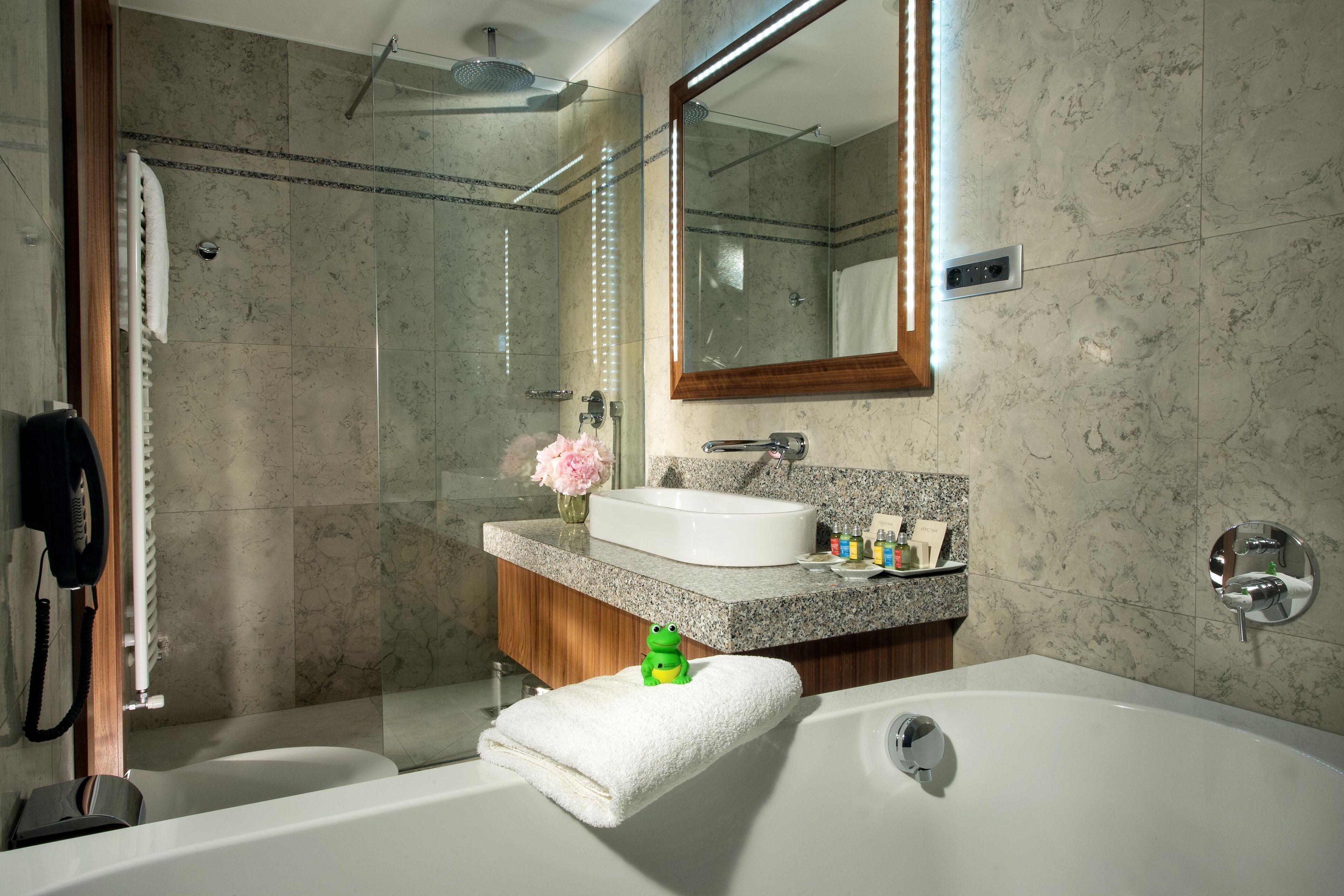 A modern bathroom with a glass-enclosed shower, a white bathtub, a vanity with a sink, and a mirror above the vanity.