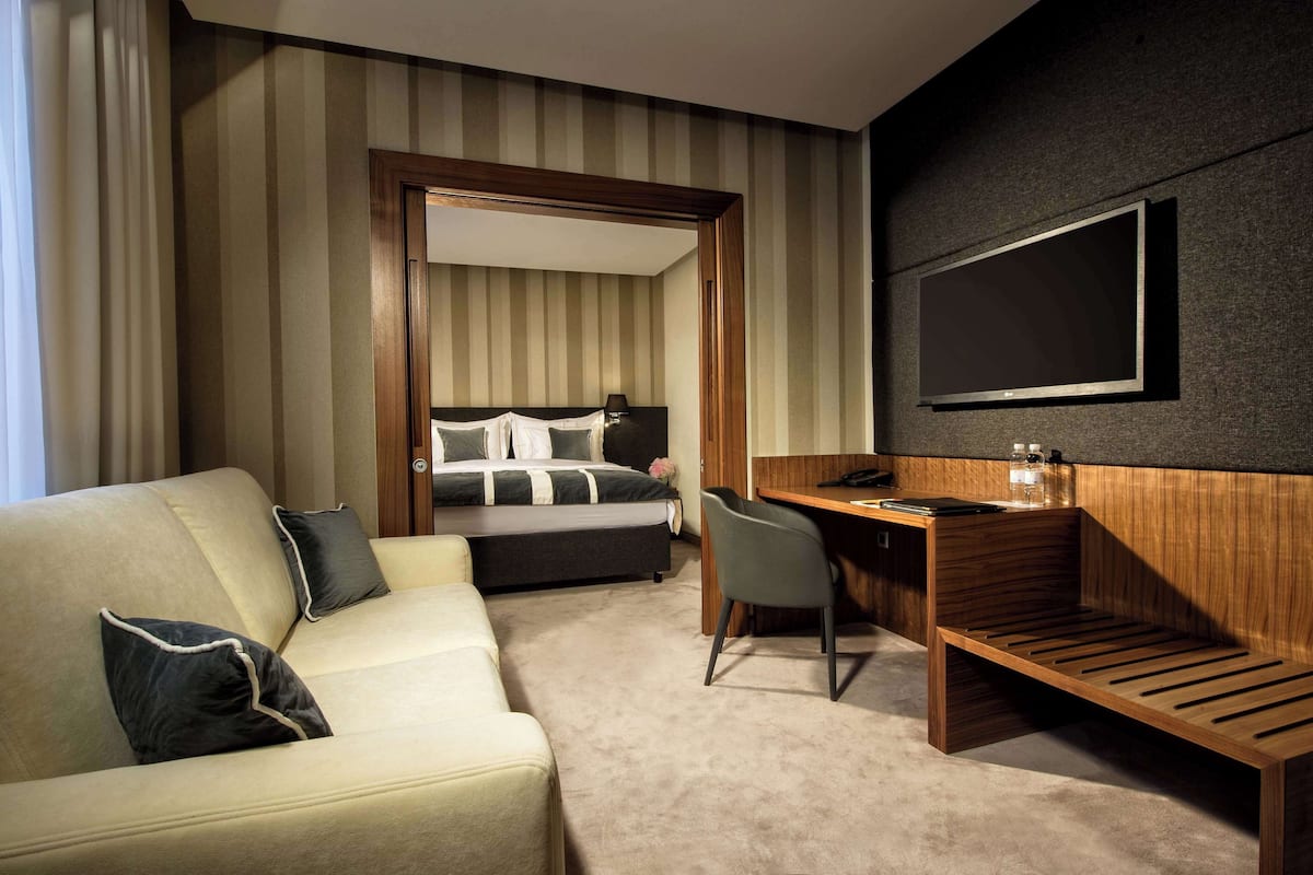 Une chambre d’hôtel avec un lit, un bureau, une chaise, une télévision et un canapé.