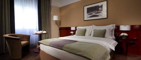 Een hotelkamer met een groot bed, een stoel, een nachtkastje met een lamp en een lijst aan de muur.