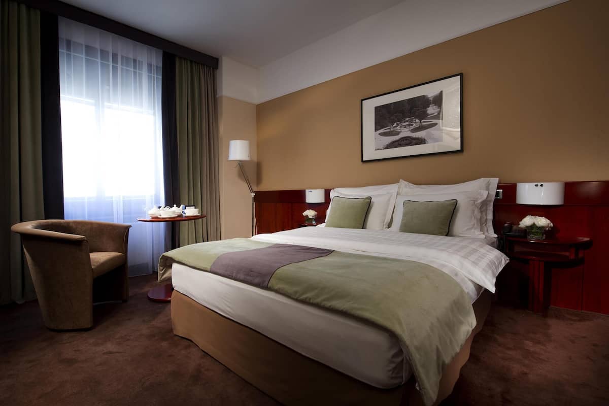 Une chambre d’hôtel avec un grand lit, une chaise, une table de chevet avec une lampe et un tableau encadré au mur.