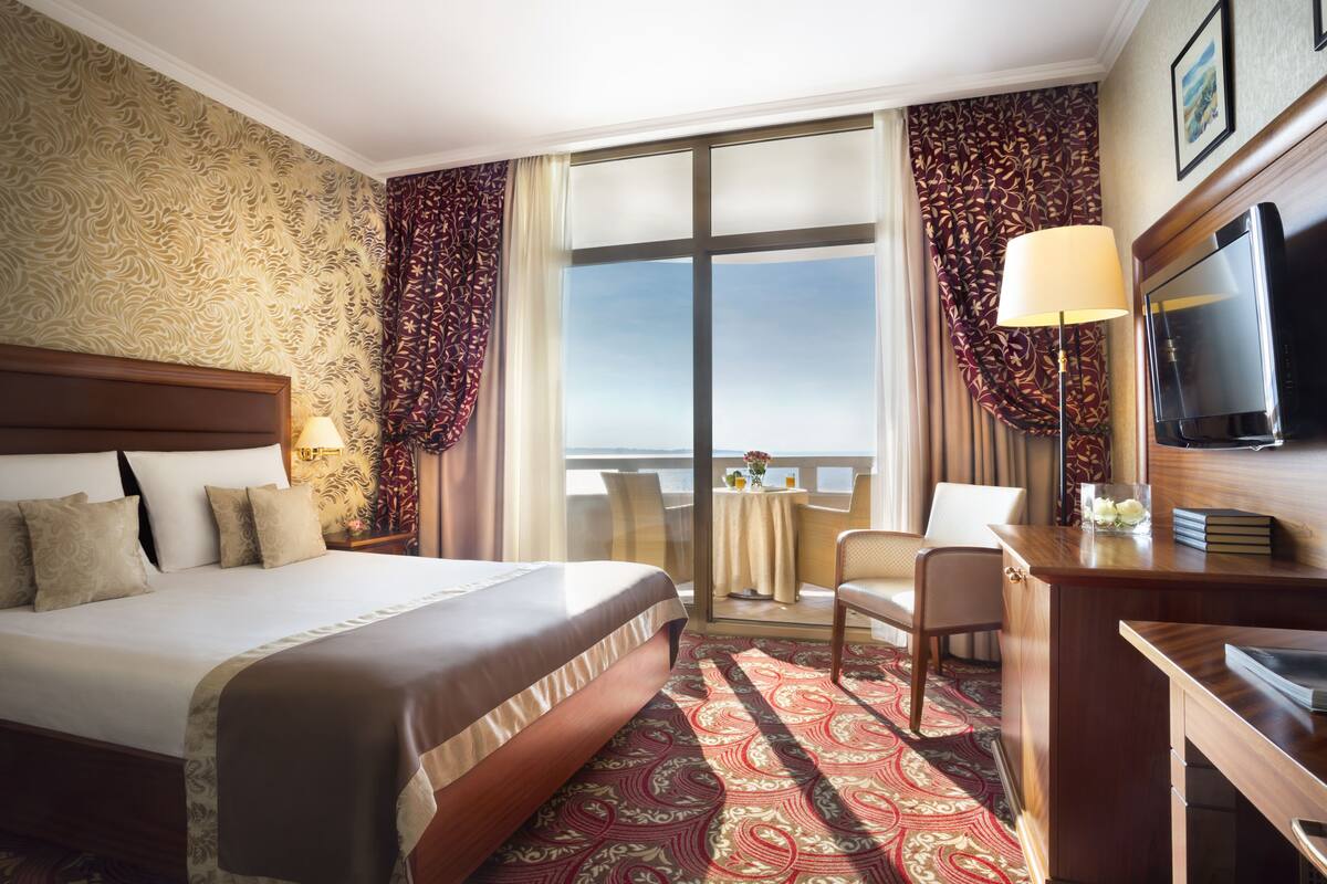 A hotel room with a large bed, a desk, a television, and a view of the ocean.