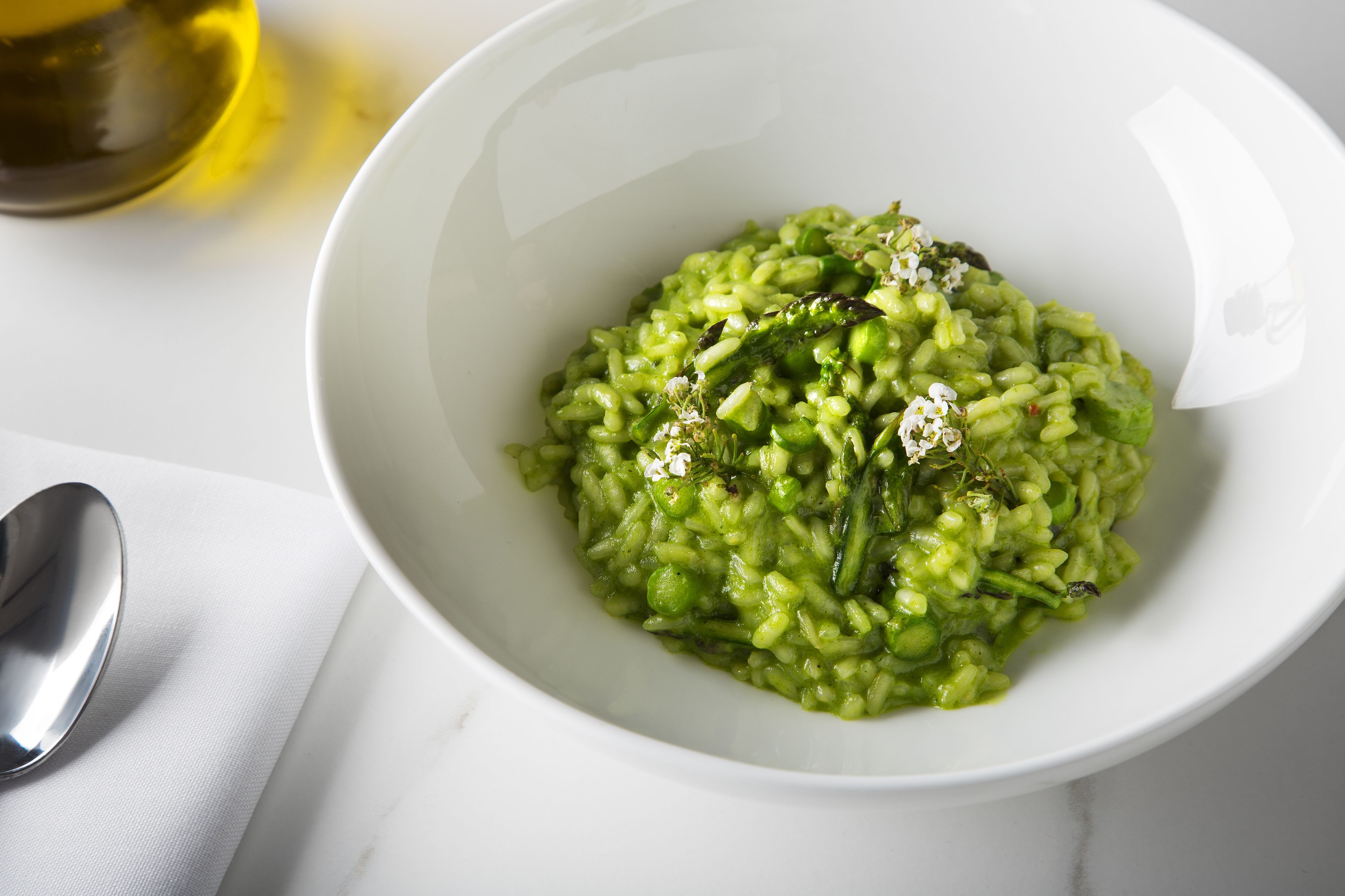 A bowl of green risotto with herbs and a spoon beside it.