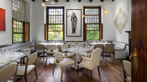 A dining area with a large table set for a meal, surrounded by chairs, with a view of the outdoors through large windows. - The Alphen Boutique Hotel & Spa (Cape Town)