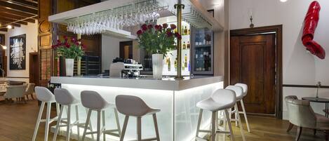 Zona de bar moderna con mostrador blanco, varios taburetes y una estantería para vinos.