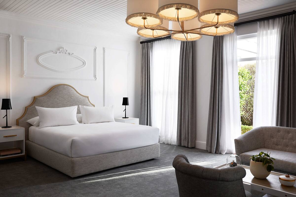 A modern hotel room with a large bed, a sofa, a chair, a nightstand, and a chandelier.