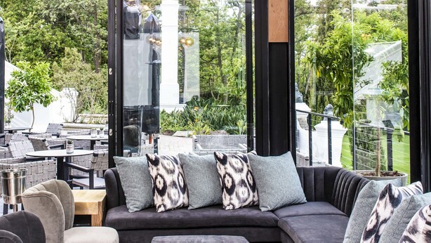 A modern outdoor seating area with a sofa, chairs, and ottomans, featuring a geometric patterned rug and a ceiling light fixture. - The Alphen Boutique Hotel & Spa (Cape Town)