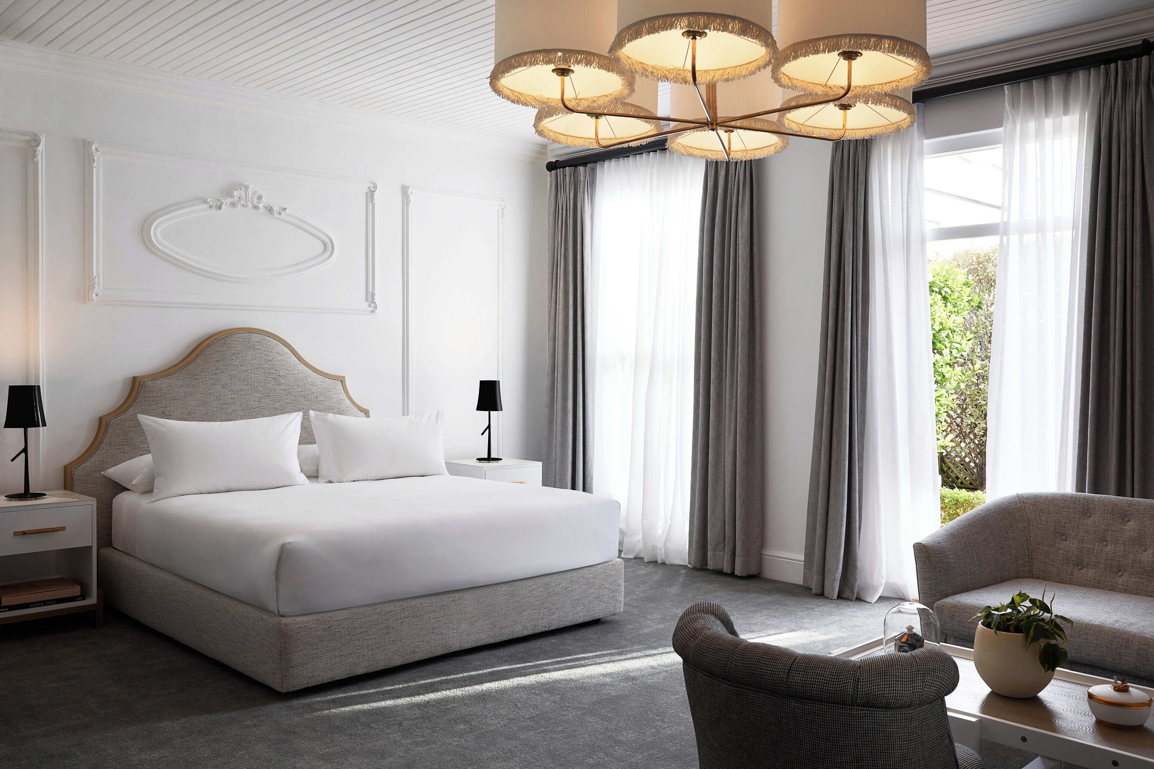 Ett modernt hotellrum med en stor säng, en soffa, en fåtölj, ett nattduksbord och en kristallkrona.