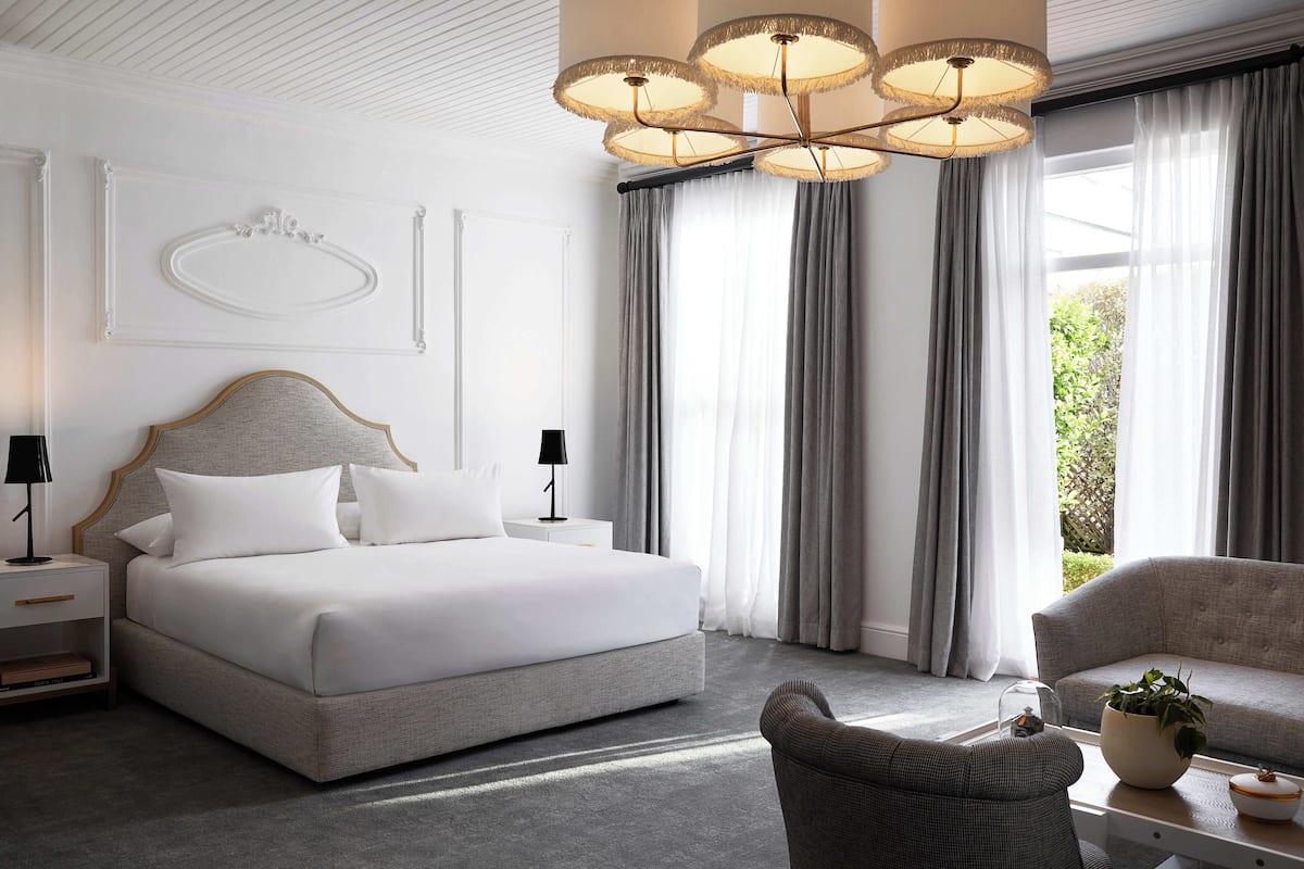 A modern hotel room with a large bed, a sofa, a chair, a nightstand, and a chandelier.