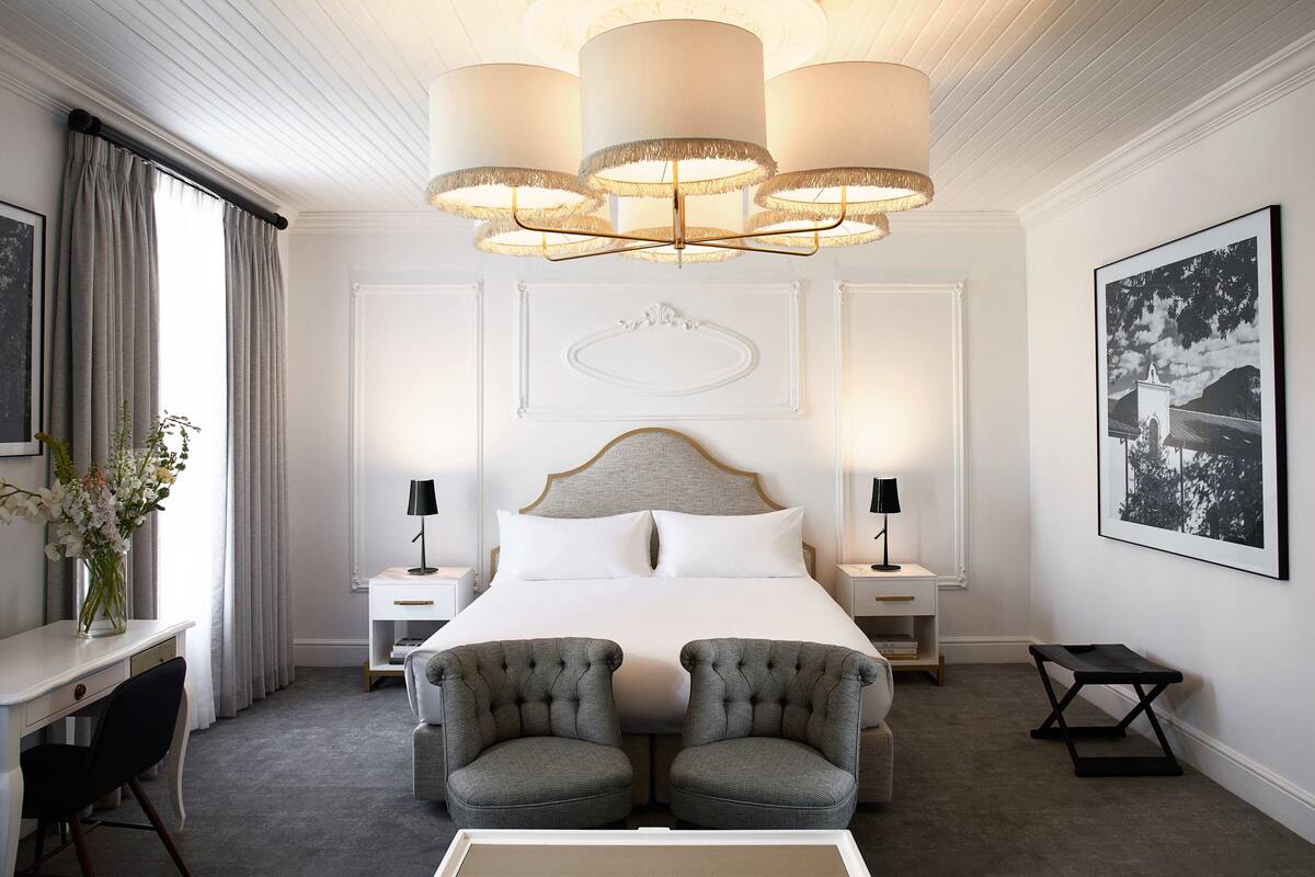 A hotel room with a large bed, two armchairs, a desk, and a chandelier.