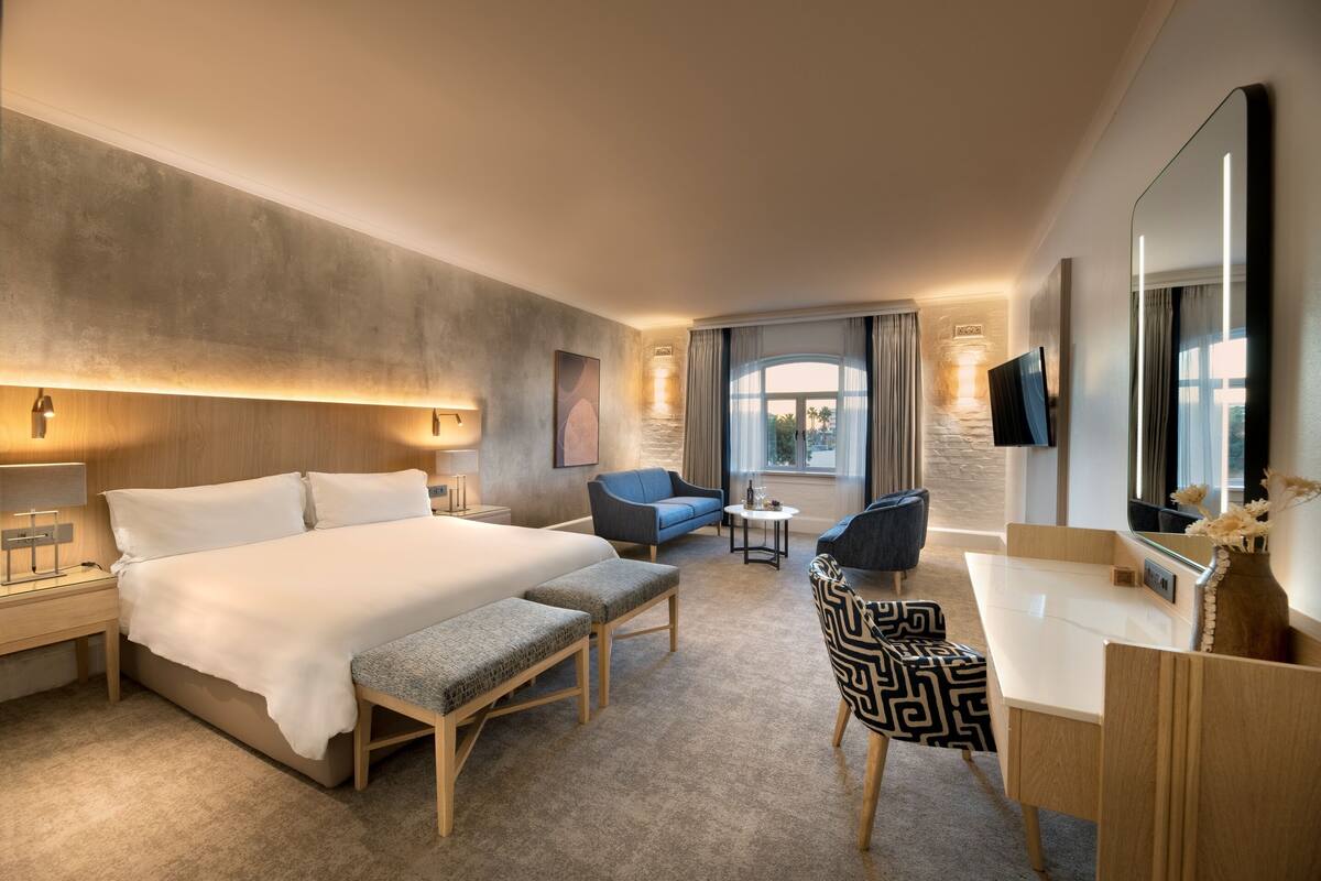 A modern hotel room with a large bed, a desk, a chair, and a sofa.