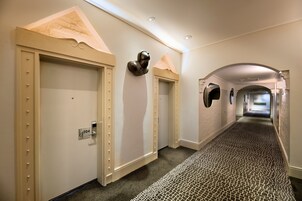 A hallway with a patterned carpet, a door with a lock, and a wall-mounted sculpture.