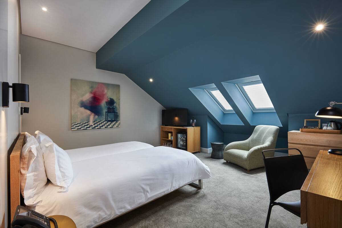 A modern bedroom with a large bed, a desk, a chair, a television, and a skylight.