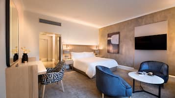 A modern hotel room with a bed, a desk with a chair, a small table, and a TV.