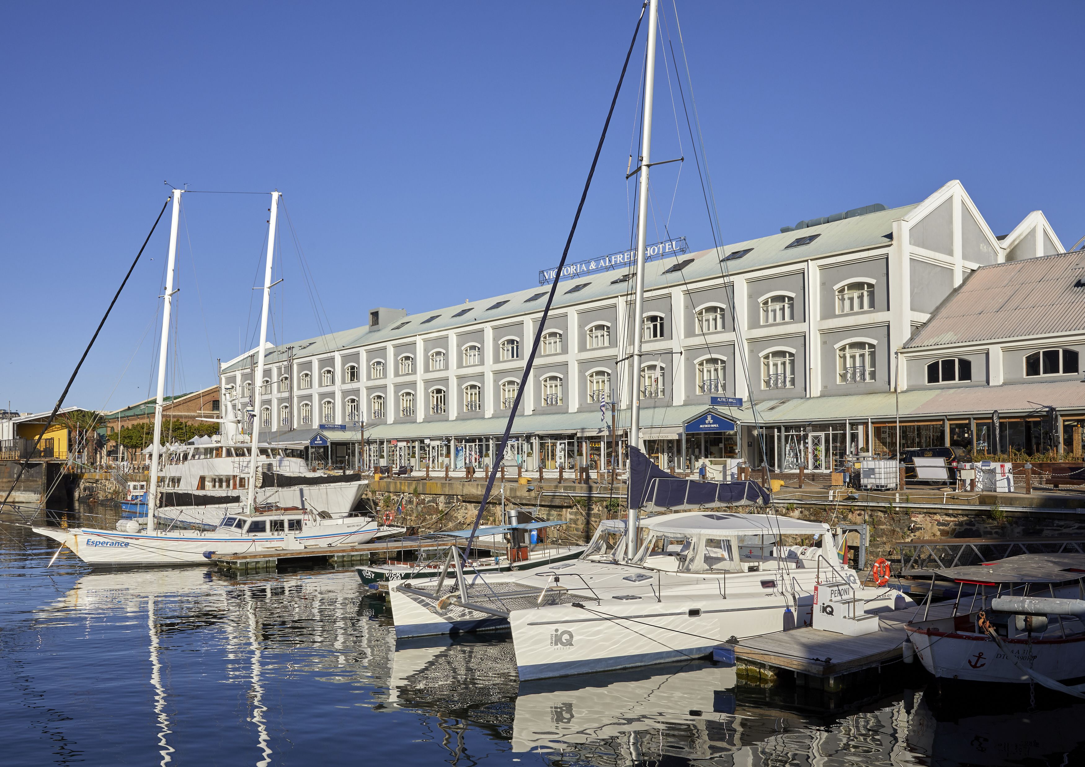 Un port de plaisance où sont amarrés plusieurs bateaux, un grand bâtiment doté de nombreuses fenêtres et de balcons, et un ciel bleu dégagé.